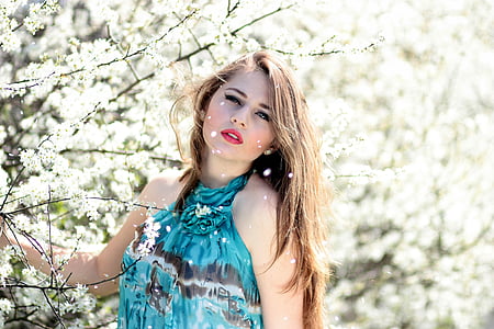 fashion photography of woman posing and wearing blue and black halter sleeveless top standing beside white flowering plants thumbnail