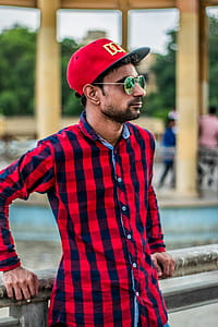 Selective Focus Photography of Man in Red and Black Gingham Sports Shirt Leaning on Grey Concrete Fence thumbnail
