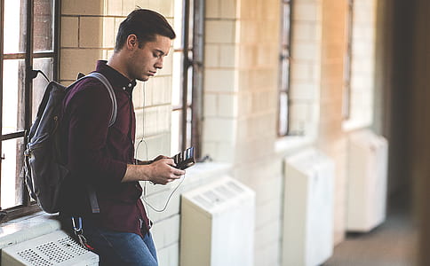 man leaning on white wall while holding phone thumbnail
