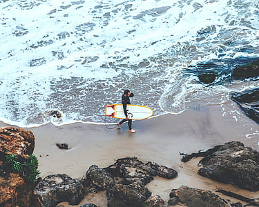 man holding surfboard while walking near seashore thumbnail