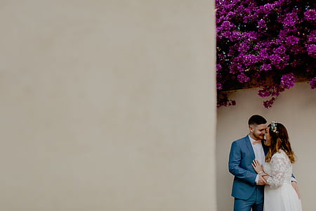 bridal couple standing beside beige wall thumbnail