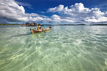 two men riding on canoe on clear body of water under white sky thumbnail