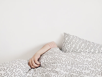 human hand on grey and white bedspread beside white wall thumbnail