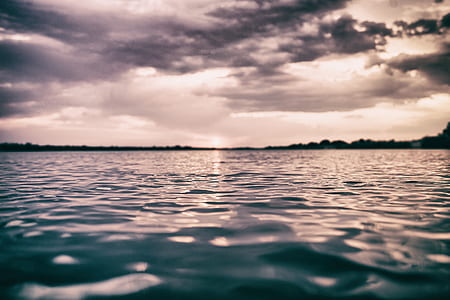 silhouette photo of calm body of water under cloudy sky thumbnail