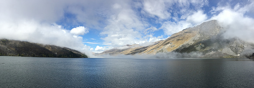large body of water near mountain under white clouds during daytime thumbnail