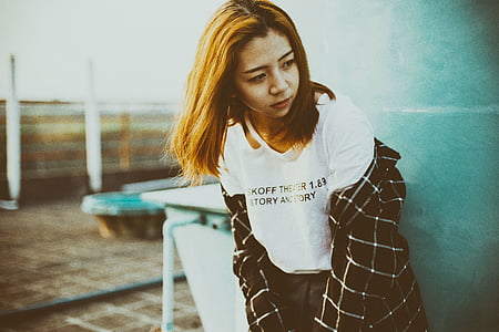woman wearing white shirt, black, bottoms, and plaid jacket leaning beside gray wall thumbnail