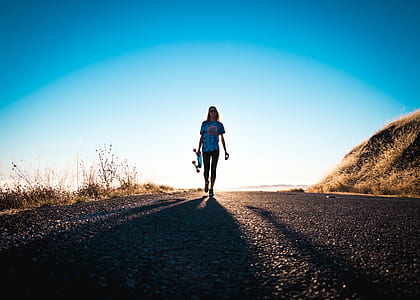 woman carrying skateboard walking on road thumbnail