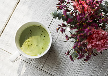 white ceramic cup filled with green syrup beside pink petaled flowers thumbnail