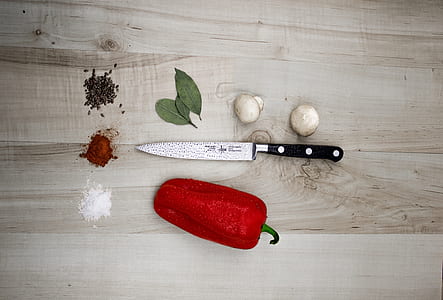 red bell peppers and gray kitchen knife on top of beige wood plank table thumbnail