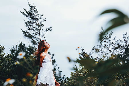 woman wearing white sundress looking up between green leaf plants thumbnail