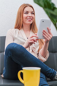 woman sitting on sofa while holding tablet computer thumbnail