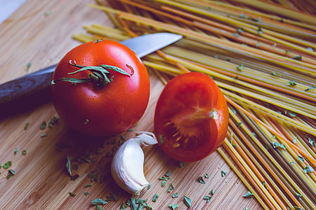 whole tomato beside sliced tomato and garlic clove on brown surface thumbnail