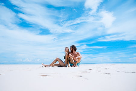 man and woman sitting on white sand under blue sky at daytime thumbnail