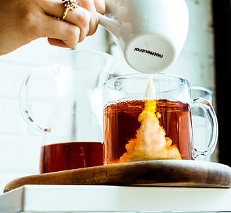 person pouring creamer from ceramic mug to clear glass mug with coffee thumbnail