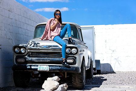 woman sitting on classic silver pickup truck beside white wall thumbnail