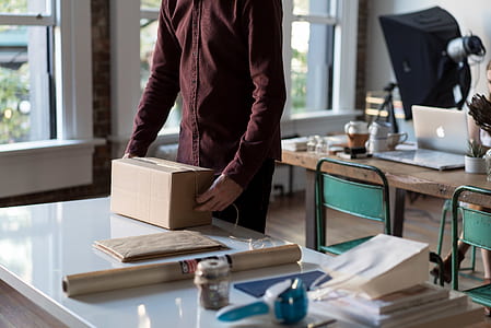 person standing near white table while holding brown box thumbnail