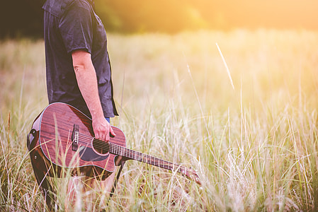 person holding guitar on grass field thumbnail