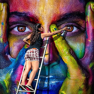 woman wearing black sleeveless shirt while spray painting in street during daytime thumbnail