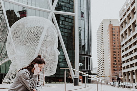woman sitting on stair while calling on smartphone near building during daytime thumbnail