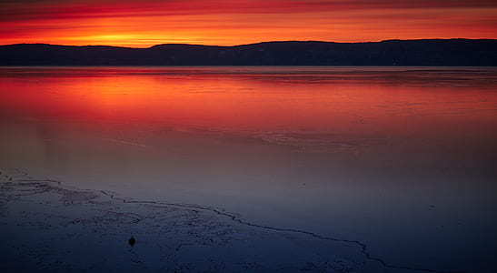silhouette of mountain across body of water during orange sunset thumbnail