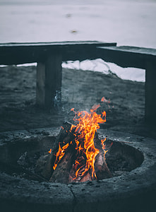 photo of firewoods burnt inside gray firepit on gray sand near body of water thumbnail