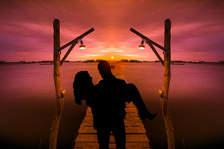 silhouette of man carrying woman on dock near water thumbnail