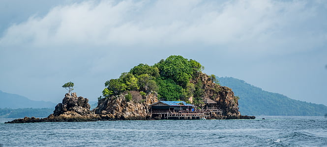 blue and white building beside rock formation surrounded by body of water thumbnail