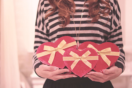 woman in black and white stripes long sleeve shirt holding three red heart-shaped boxes thumbnail