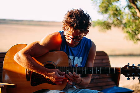 man playing his brown guitar while sitting on bench thumbnail