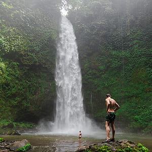 man standing on rock near waterfalls during daytime thumbnail