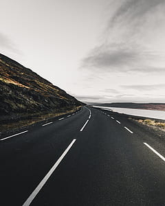 road beside hill and body of water during daytime thumbnail