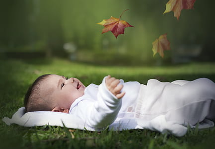 photograph of baby lying on grass with leaf smiling thumbnail