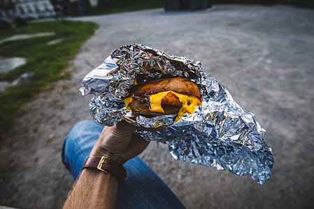 person holding foil wrapped melted cheese burger thumbnail
