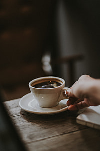 selective focus photography of person holding ceramic mug with black liquid on brown table thumbnail