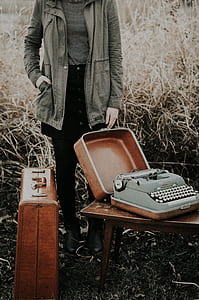 person wearing gray jacket holding brown wooden suit case with typewriter thumbnail