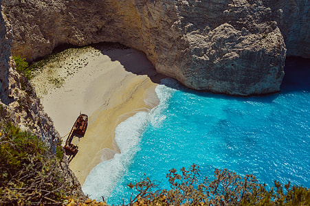 shipwreck on seashore with blue body of water surrounded by rock cliff during daytime thumbnail