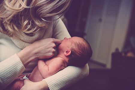 shallow focus photography of woman in white sweater carrying baby thumbnail