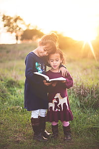 two girls reading book during daytime thumbnail
