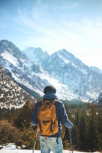 man wearing blue bubble jacket holding ski poles facing the forest thumbnail
