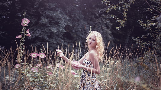 woman in black, green, and red floral tube dress standing near purple petaled floowers thumbnail