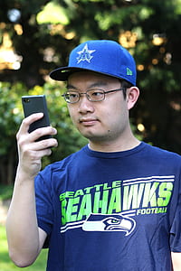 selective focus photography of man holding smartphone near green leafed trees thumbnail