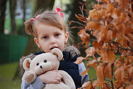 girl holding beige bear plush toy beside brown leaf thumbnail
