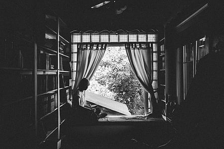 grayscale photo of woman sitting on bed near window thumbnail