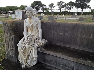 women's concrete statue sitting on black concrete bench thumbnail