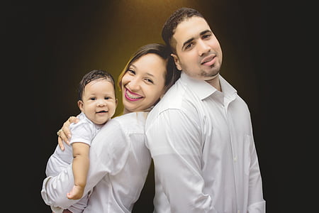 woman and man in white dress shirts leaning each other while holding a baby thumbnail