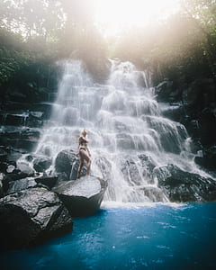 woman standing on rock beside waterfalls thumbnail