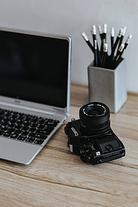 Black-and-white photos with a silver laptop, a smartphone, car keys, pencils and a camera thumbnail