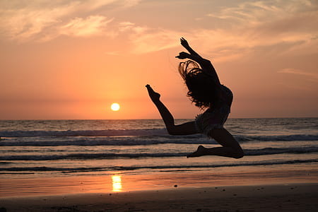 woman jumping near body of water during sunset thumbnail
