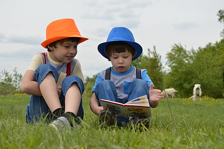 kid reading a book beside boy while sitting on grass field outdoor thumbnail