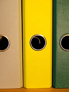 close-up of three green, yellow, and brown binders on brown surface thumbnail